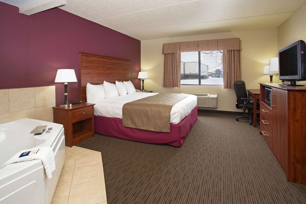 Een hotelkamer met een groot bed, een bureau, een stoel, een televisie en een badkamer met een bad.