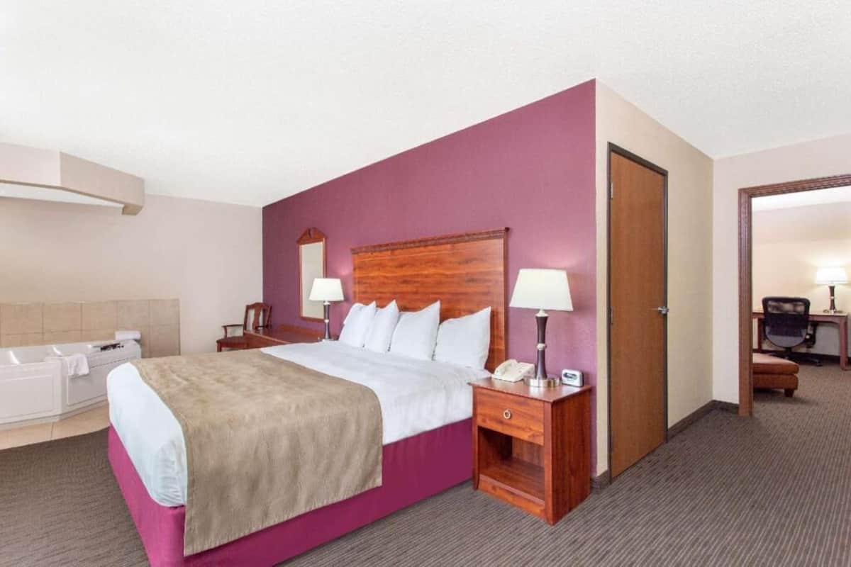 Een hotelkamer met een bed, bedlampjes, een telefoon, een bureau met een stoel, en een deur.