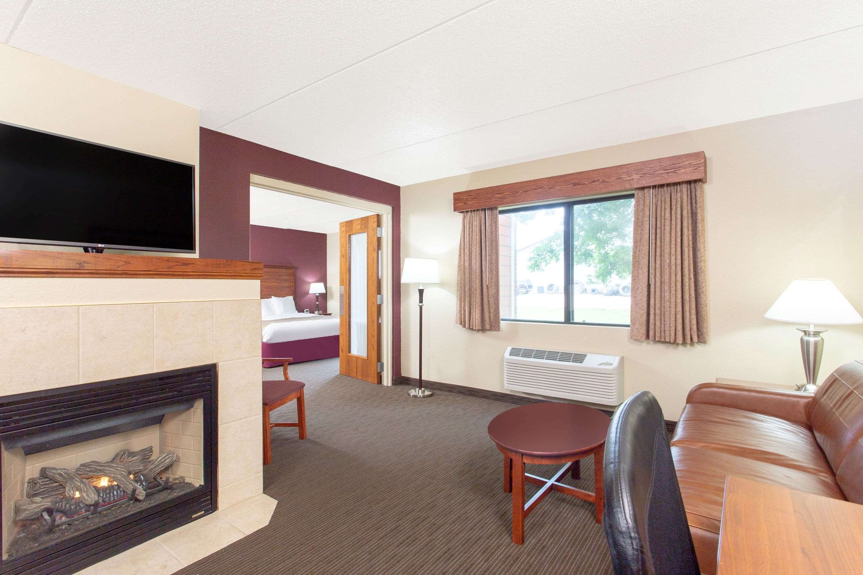 A hotel room with a fireplace, a flat-screen TV, a sofa, a table, and a window with curtains.