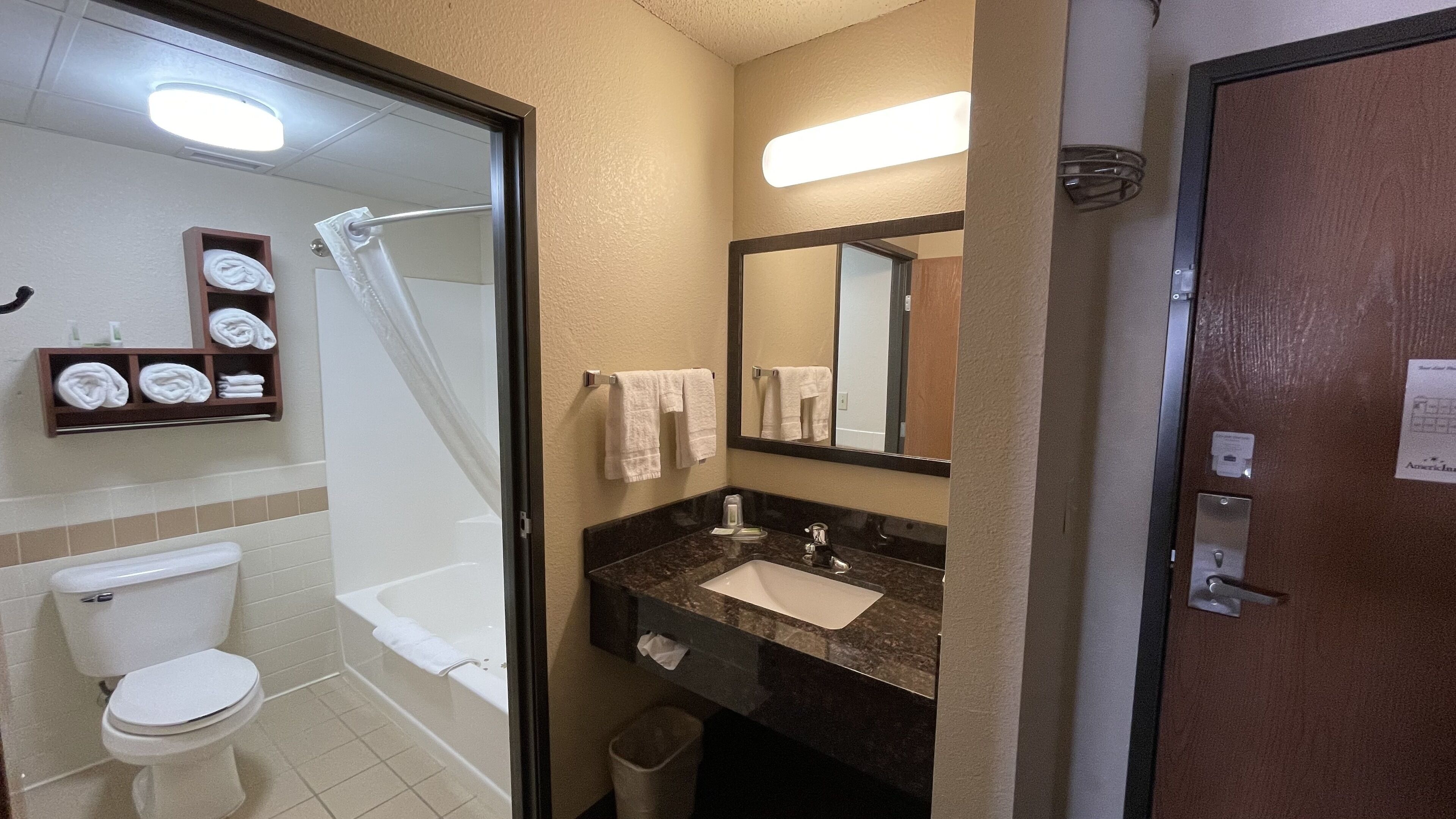 A bathroom with a toilet, a bathtub, a sink, and a shower. There are towels and toiletries on the wall.