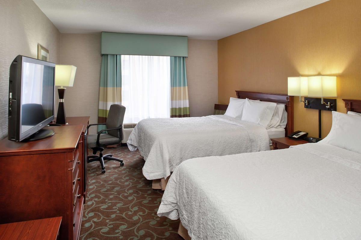 A hotel room with two beds, a desk with a television, a chair, and a desk lamp.