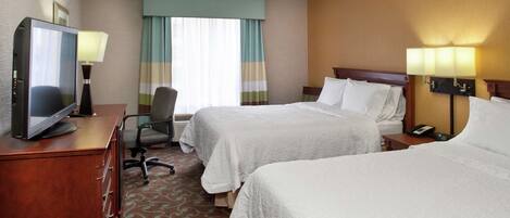 A hotel room with two beds, a desk with a television, a chair, and a desk lamp.