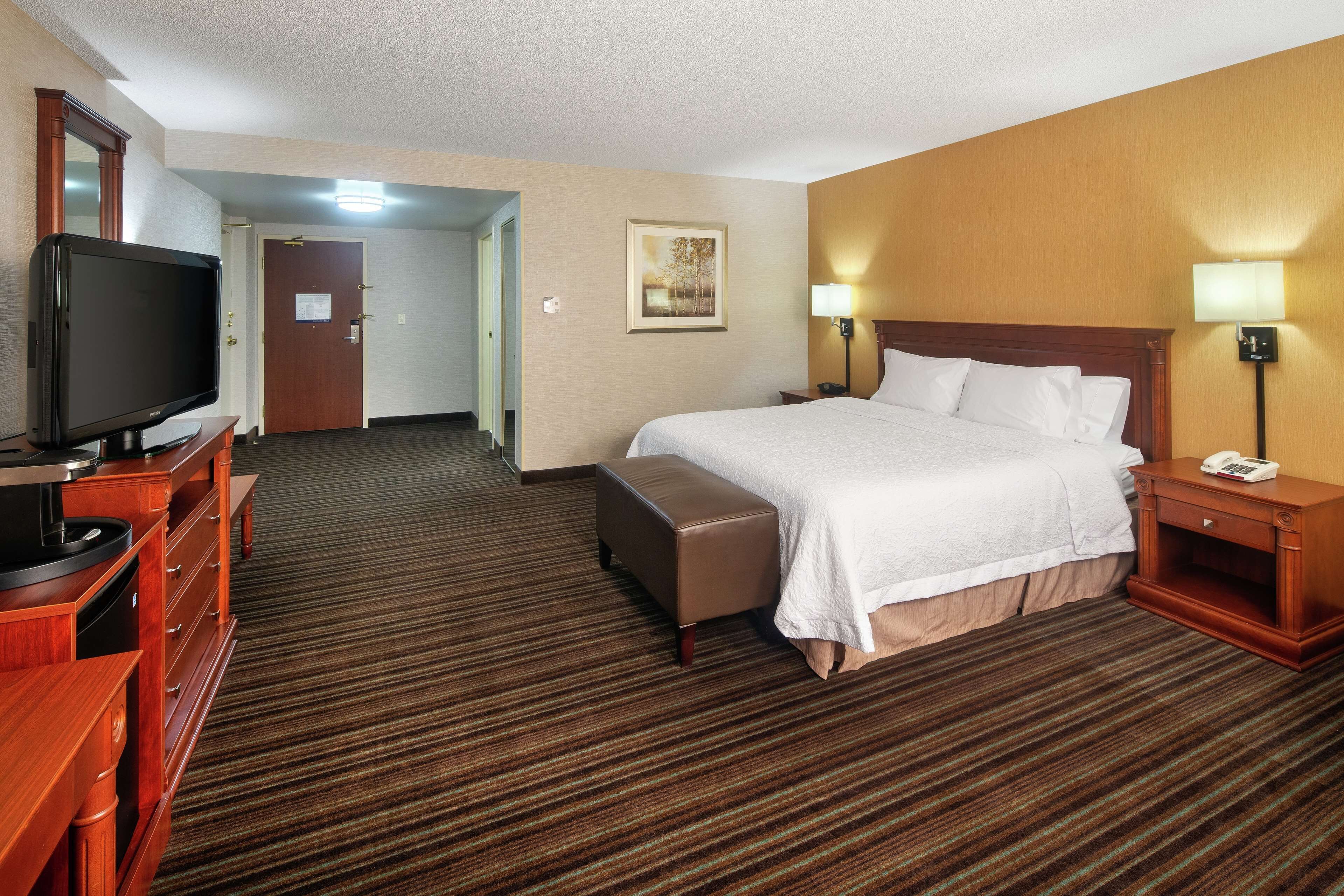 A hotel room with a bed, a TV, a desk with drawers, a lamp, and a painting on the wall.