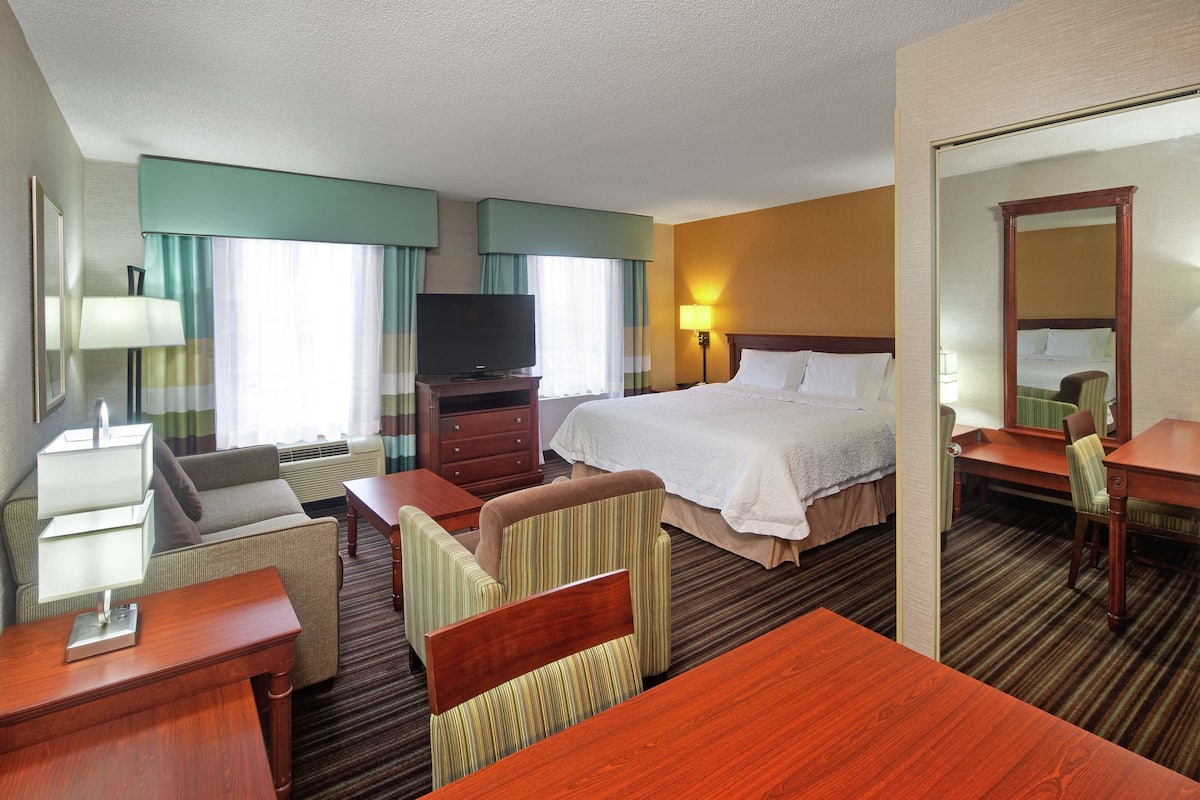 A hotel room with a bed, a desk, a chair, a television, and a lamp.