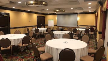 A conference room with round tables, chairs, a projector screen, and a whiteboard.