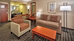 A hotel room with a living area featuring a sofa, armchairs, a coffee table, a dining table, and a mirror. - Hampton Inn & Suites by Hilton Toronto Airport (Mississauga)