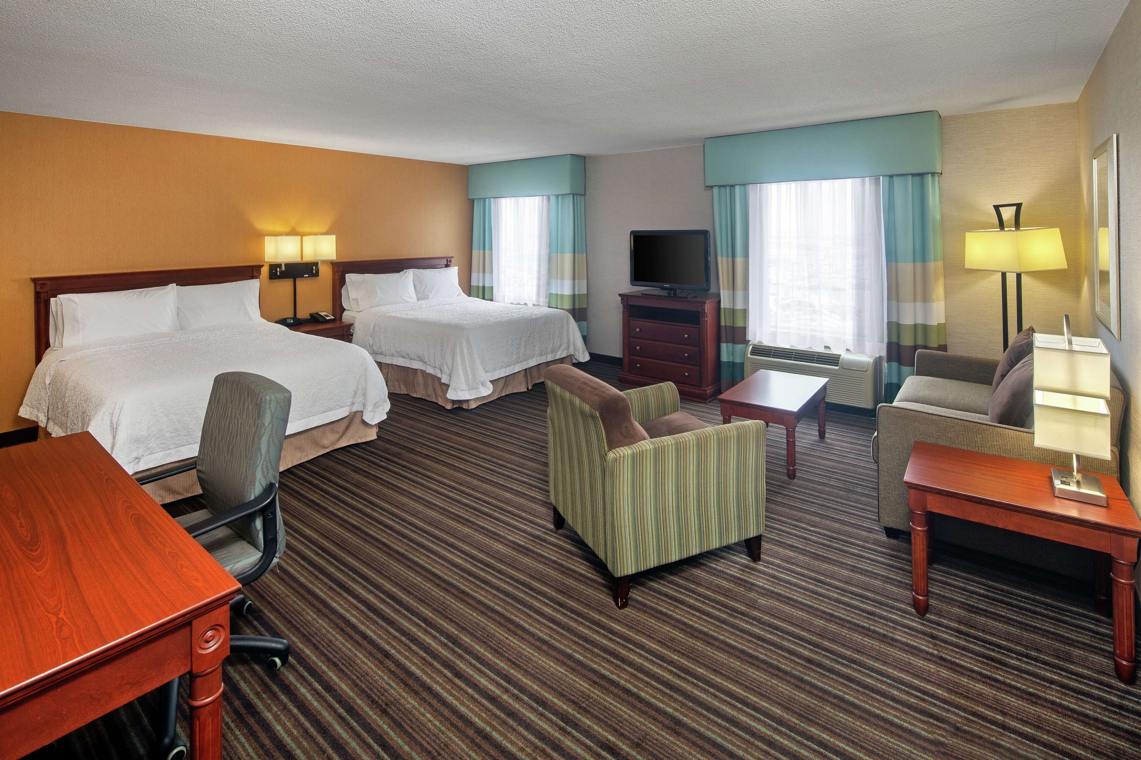 A hotel room with two beds, a desk, a chair, a television, and a sofa.