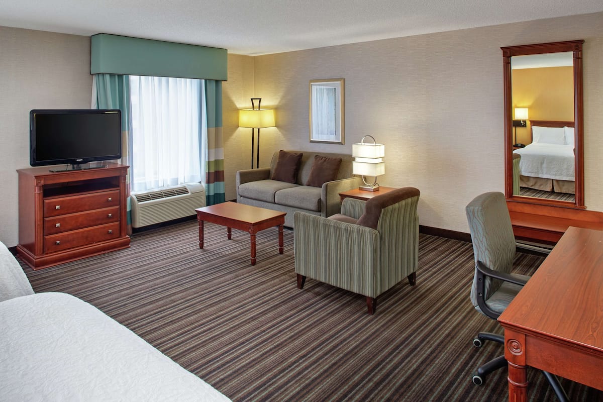 A hotel room with a bed, a television on a wooden cabinet, a sofa, a desk, and a chair.