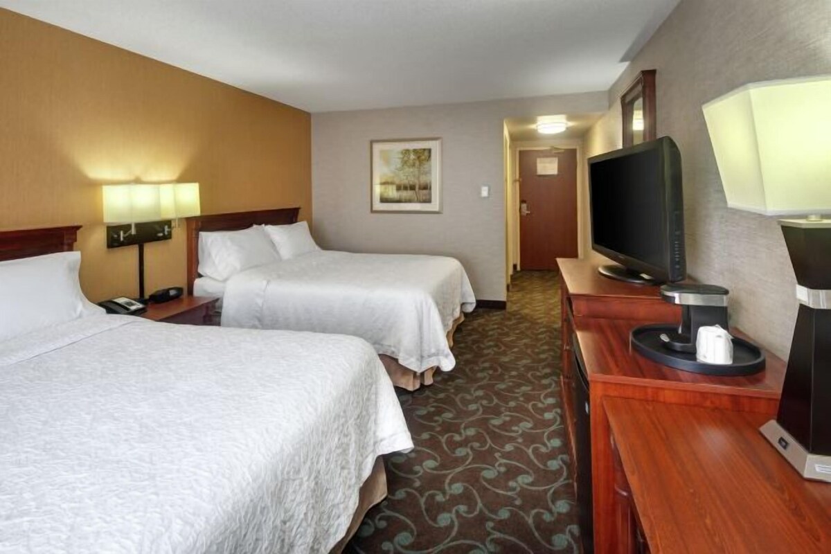 A hotel room with two beds, a TV, a coffee maker, and a lamp.