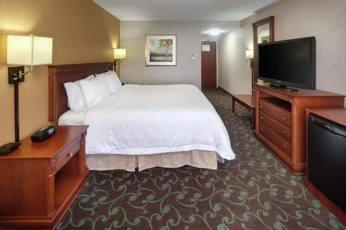 A hotel room with a large bed, bedside lamps, a TV, a desk with a phone, and a carpeted floor.