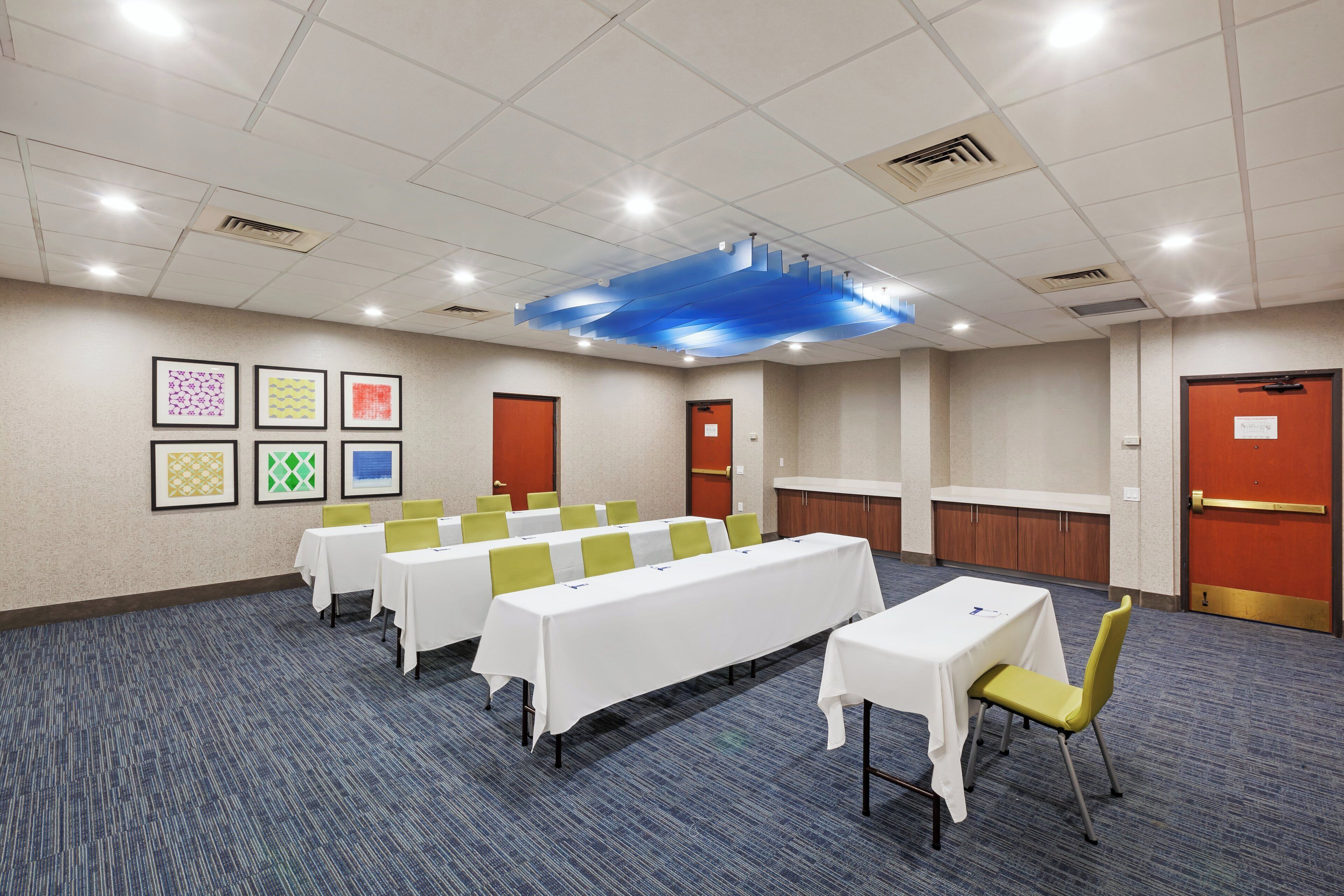 Une salle de conférence dotée de plusieurs tables et chaises, d’un tapis à motifs et d’un plafond équipé d’un système d’éclairage encastré.