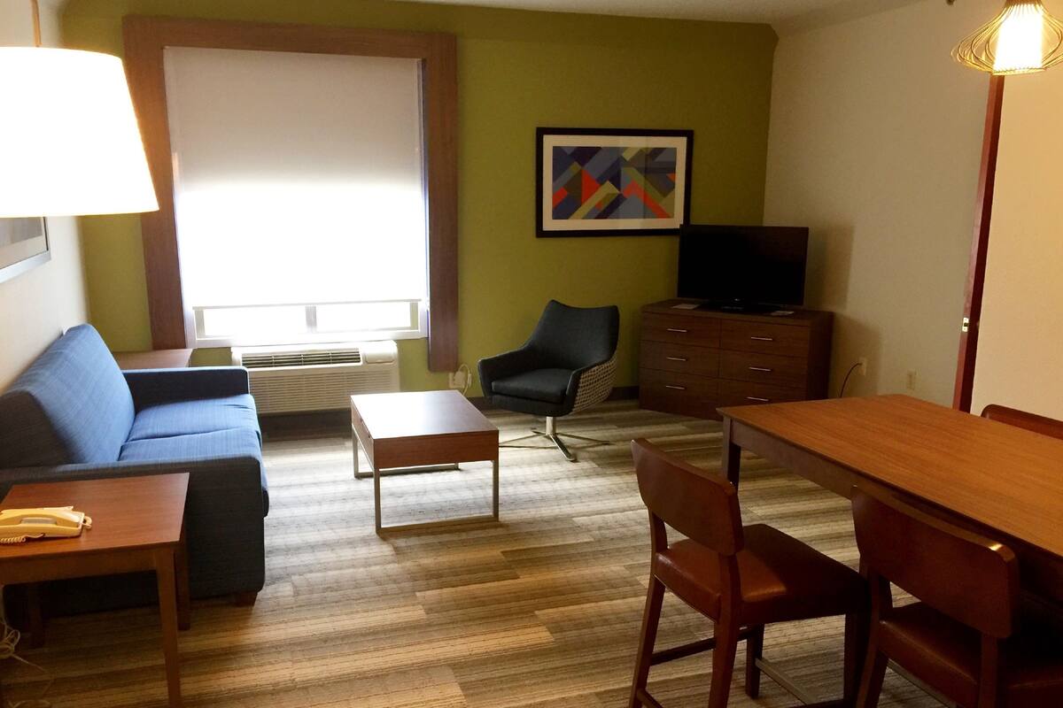 Ein möbliertes Wohnzimmer mit Sofa, Couchtisch, Fernseher, Sessel, Holztisch und Kommode.