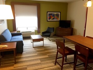A furnished living room with a sofa, a coffee table, a TV, a chair, a wooden table, and a dresser. - Holiday Inn Express & Suites Houston - Memorial Park Area by IHG (Houston)