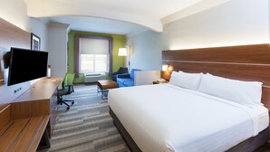 Une chambre d’hôtel avec un grand lit, un bureau doté d’un téléviseur à écran plat, une chaise, une lampe et une fenêtre avec des stores.