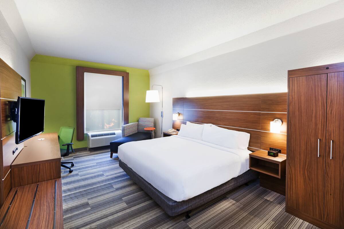 Ein Hotelzimmer mit einem großen Bett, einem Schreibtisch mit Flachbildfernseher, einem Sessel, einer Schreibtischlampe und einem Kleiderschrank.