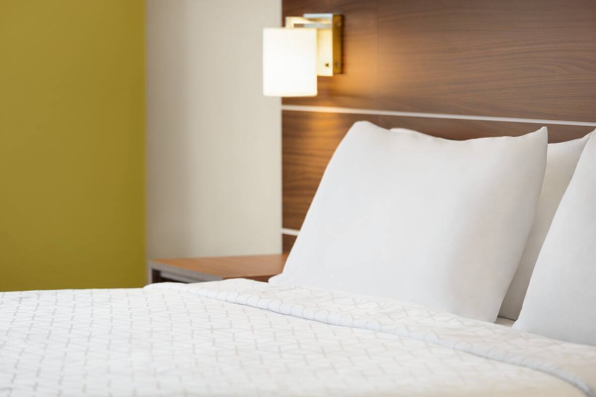 A hotel room with a neatly made bed, a wooden headboard, and a wall-mounted light fixture.
