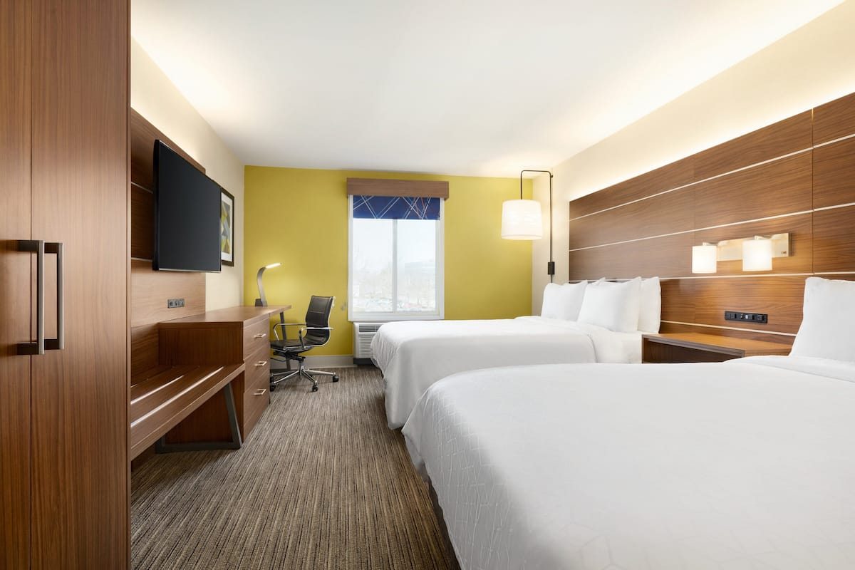 A hotel room with two beds, a desk, a chair, a television, and a window.