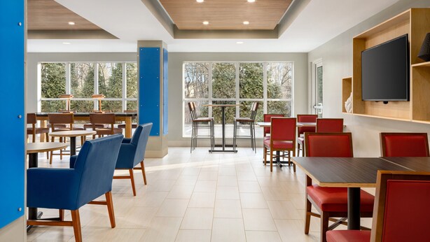 A modern dining area with multiple tables and chairs, large windows, and a flat-screen TV mounted on the wall. - Holiday Inn Express & Suites Philadelphia - Mt. Laurel by IHG (Mount Laurel)