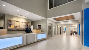 A modern hotel reception area with a reception desk, a man standing behind it, and a view of the hotel's interior. - Holiday Inn Express & Suites Philadelphia - Mt. Laurel by IHG (Mount Laurel)