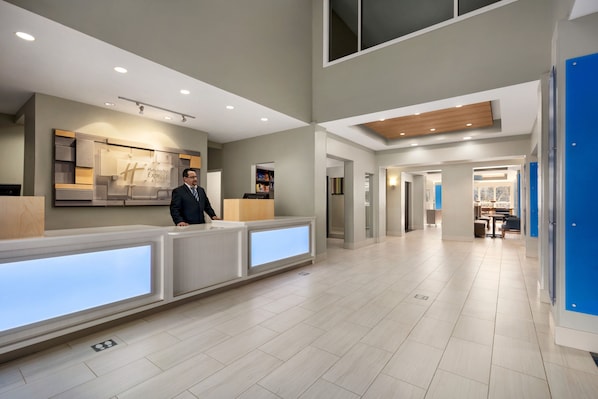 A modern hotel reception area with a reception desk, a man standing behind it, and a view of the hotel's interior. - Holiday Inn Express & Suites Philadelphia - Mt. Laurel by IHG (Mount Laurel)