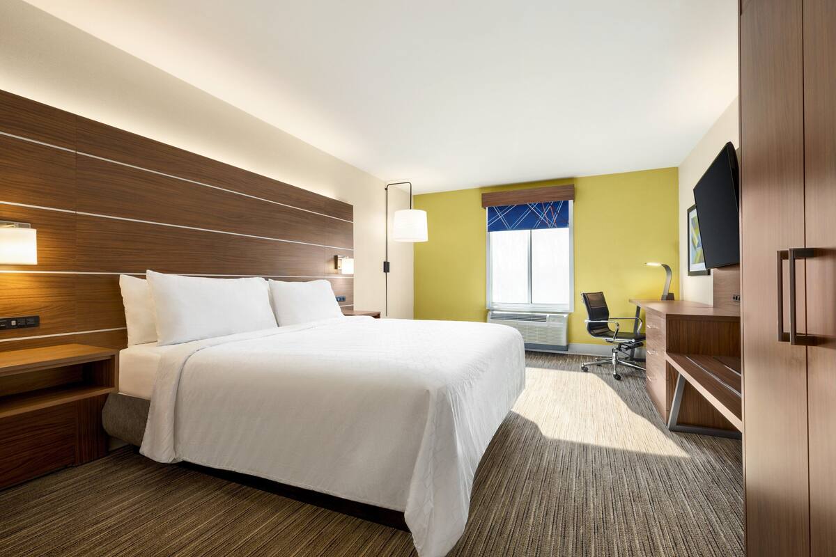 A hotel room with a large bed, a desk, a chair, and a TV.