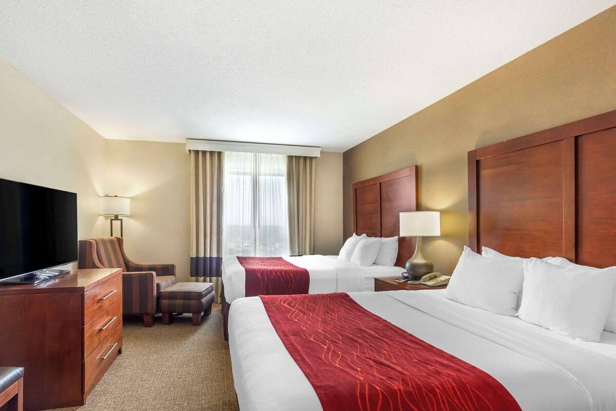 A hotel room with two beds, a desk, a TV, and a window with curtains.