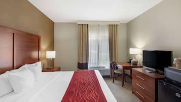 A hotel room with a large bed, a desk with a television, a refrigerator, and a window with curtains.