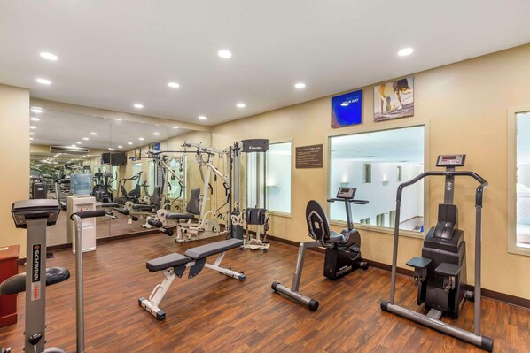 A gym with various exercise equipment, including treadmills, weight machines, and a bench.