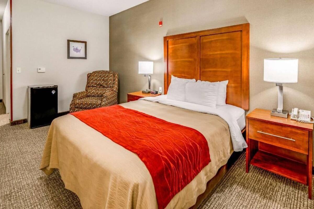 A hotel room with a large bed, two bedside tables, a chair, a small desk, and a wall-mounted picture.