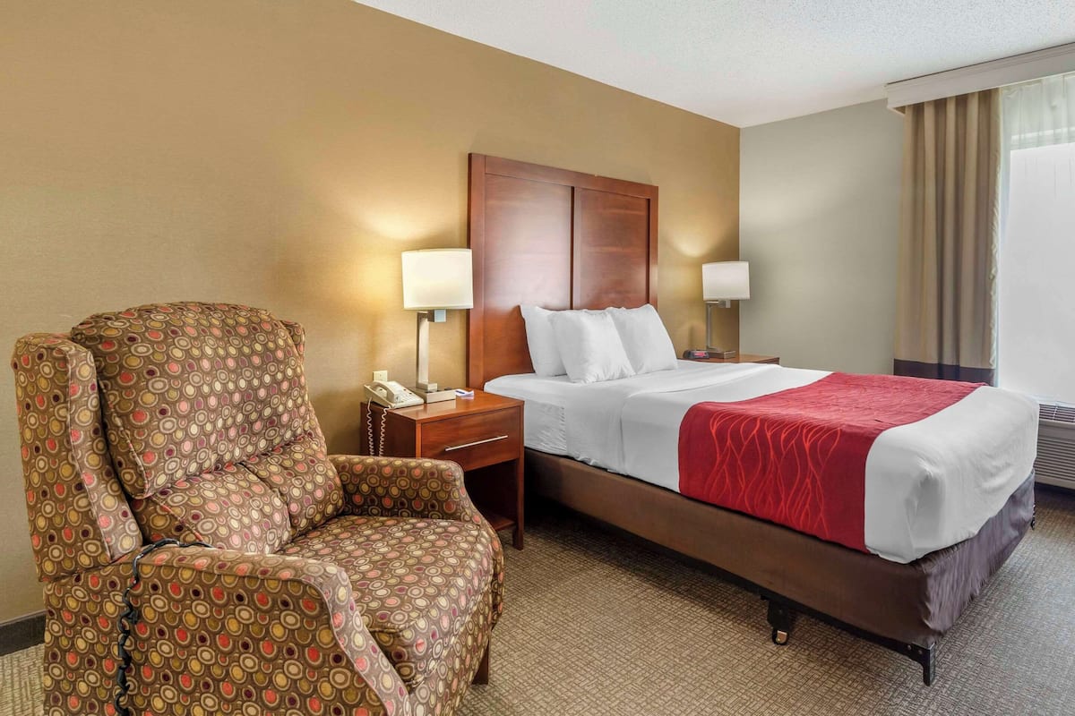 A hotel room with a bed, a chair, a nightstand, and a lamp.