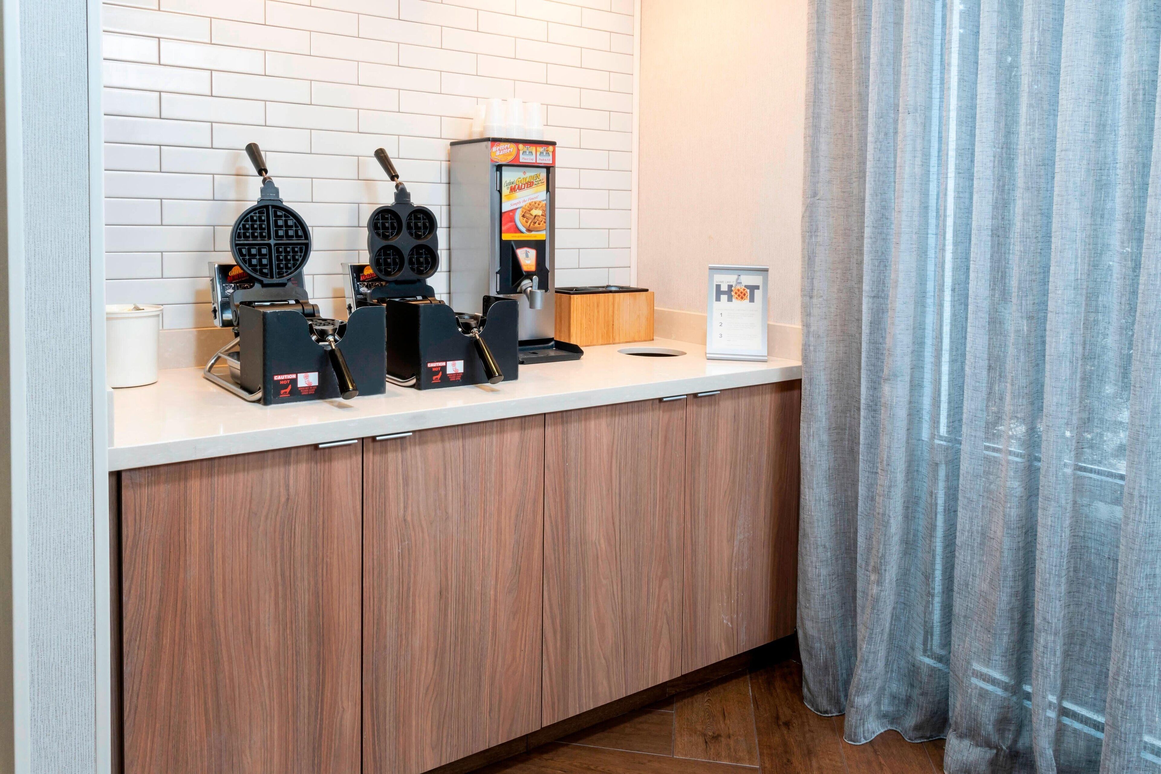 Angolo cottura con piastra per waffle, macchina del caffè e bacheca con il menu.