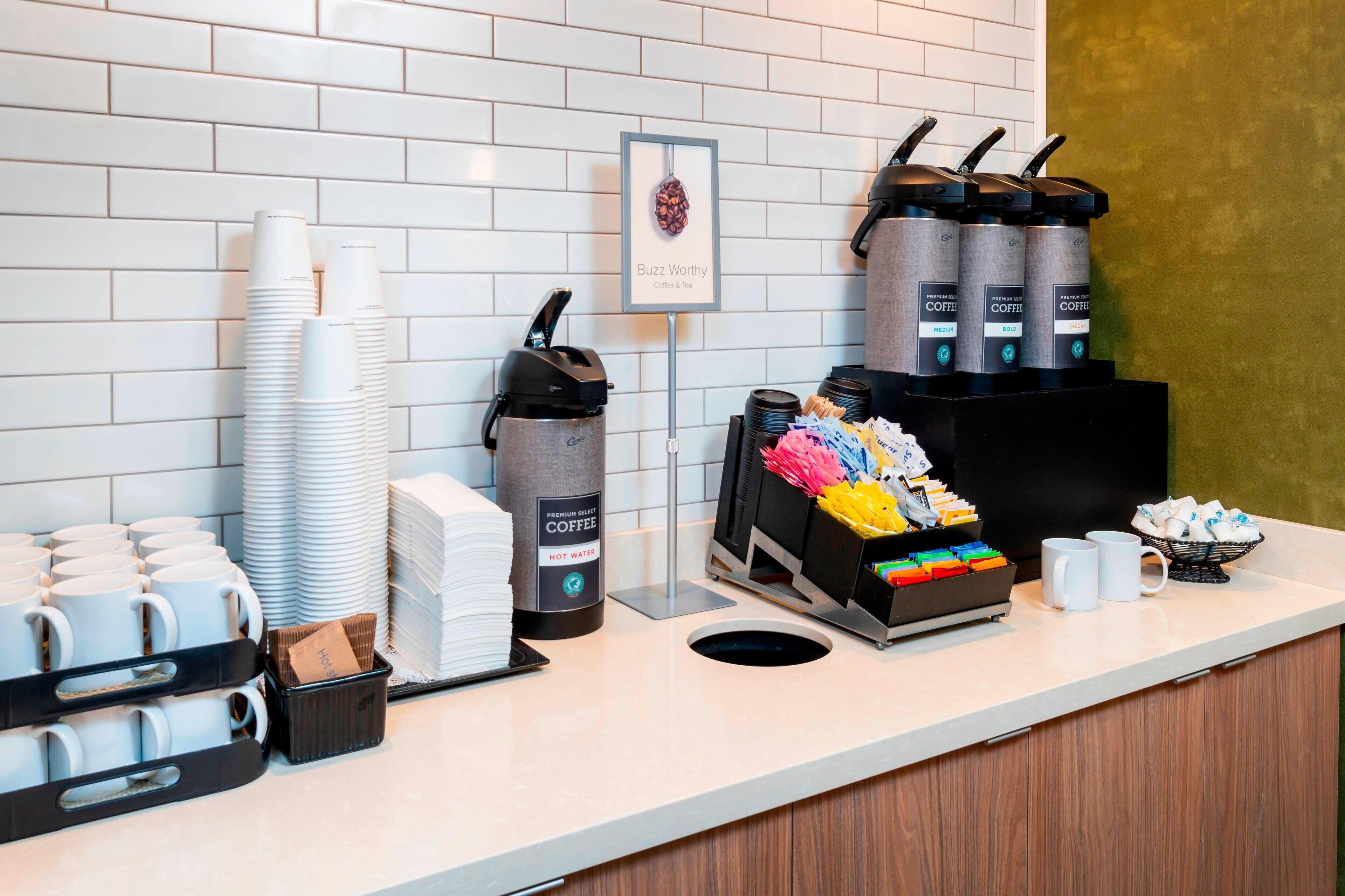Een koffiehoek met stapels wegwerpbekers, een koffieapparaat en een koffieautomaat.