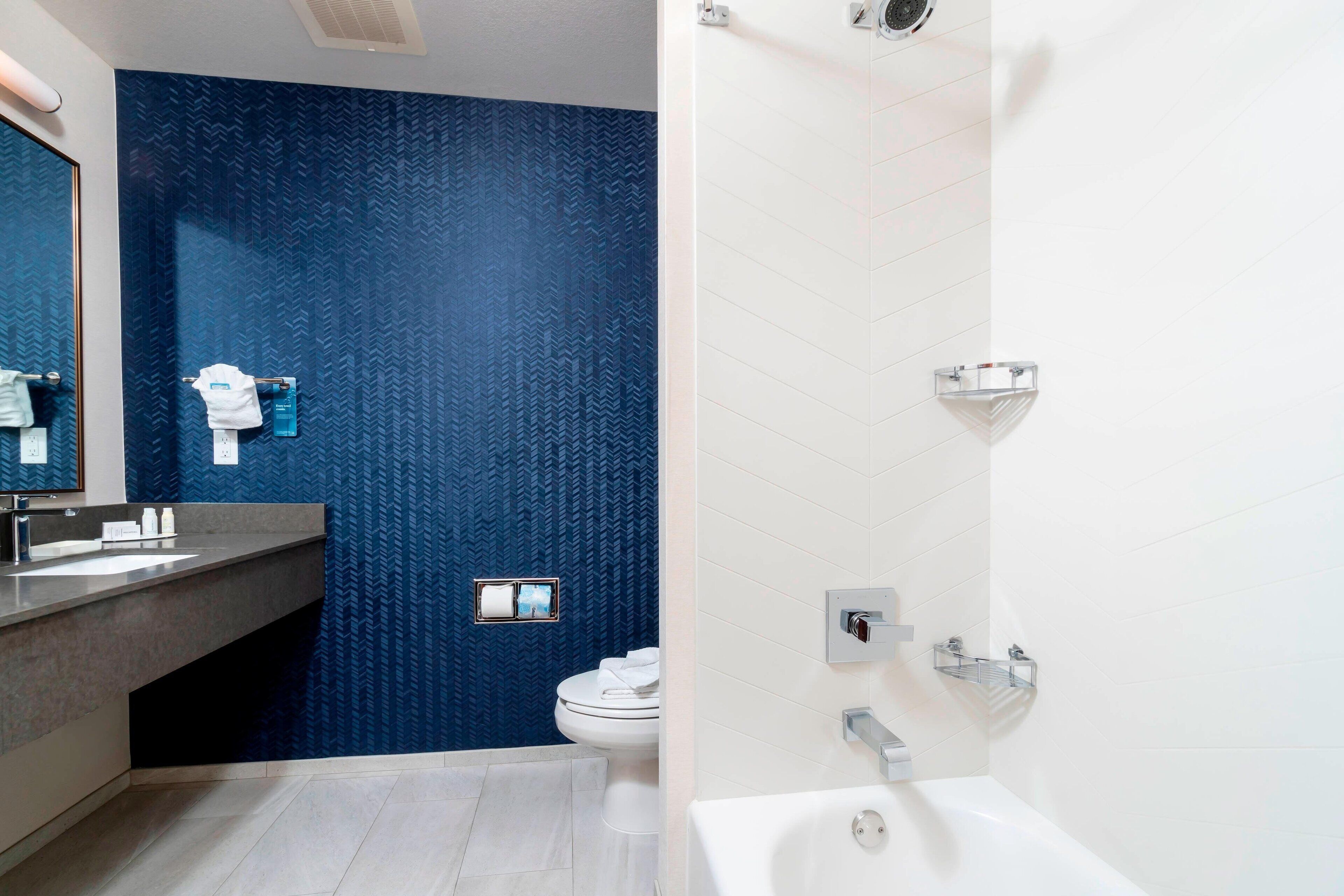 A modern bathroom with a blue textured wall, a white sink, a toilet, and a bathtub.
