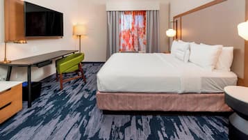 A hotel room with a bed, desk, chair, TV, and a window with curtains.