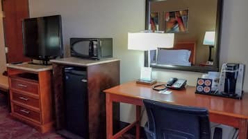 Een hotelkamer met een bureau, een televisie, een magnetron, een koffiezetapparaat, een telefoon en een spiegel.