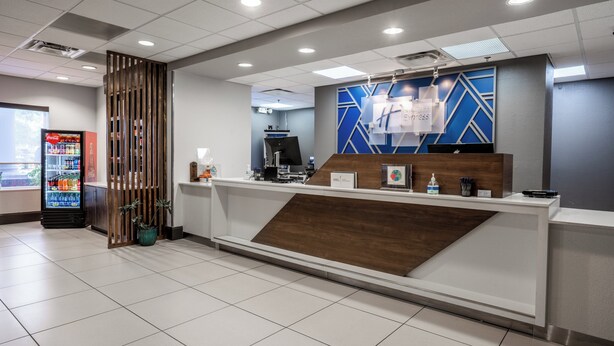 A hotel reception area with a modern design, including a reception desk, a Coca-Cola refrigerator, and a decorative plant. - Holiday Inn Express & Suites Orange City - Deltona by IHG (Orange City)