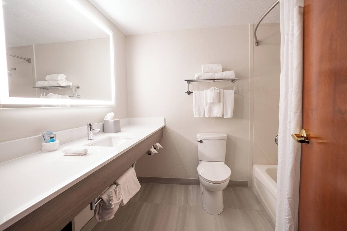 A modern bathroom with a white sink, toilet, and shower. There is a towel rack above the toilet and a towel hanging on the wall.