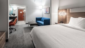 A hotel room with a large bed, a desk with a chair, a blue sofa, and a small table. - Holiday Inn Express & Suites Orange City - Deltona by IHG (Orange City)