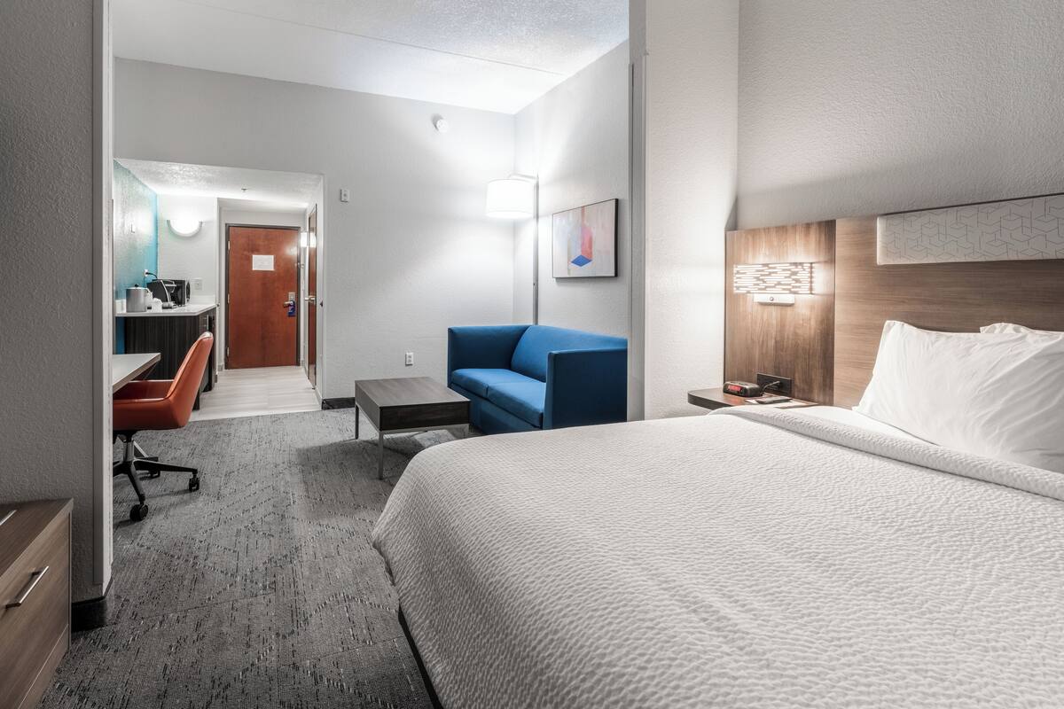 A hotel room with a large bed, a desk with a chair, a blue sofa, and a small table.