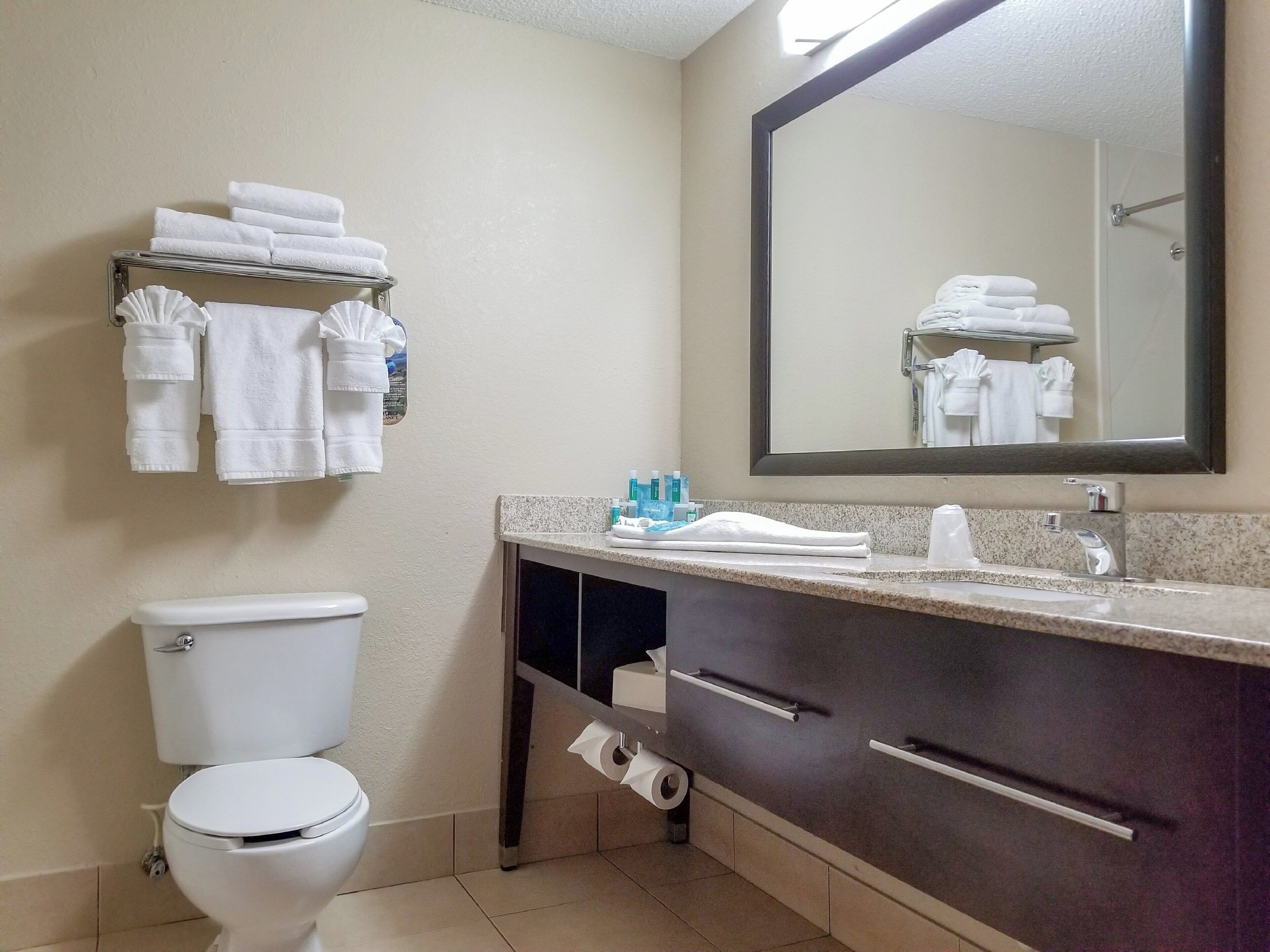 A bathroom with a toilet, a sink with a mirror, and a towel rack with folded towels.