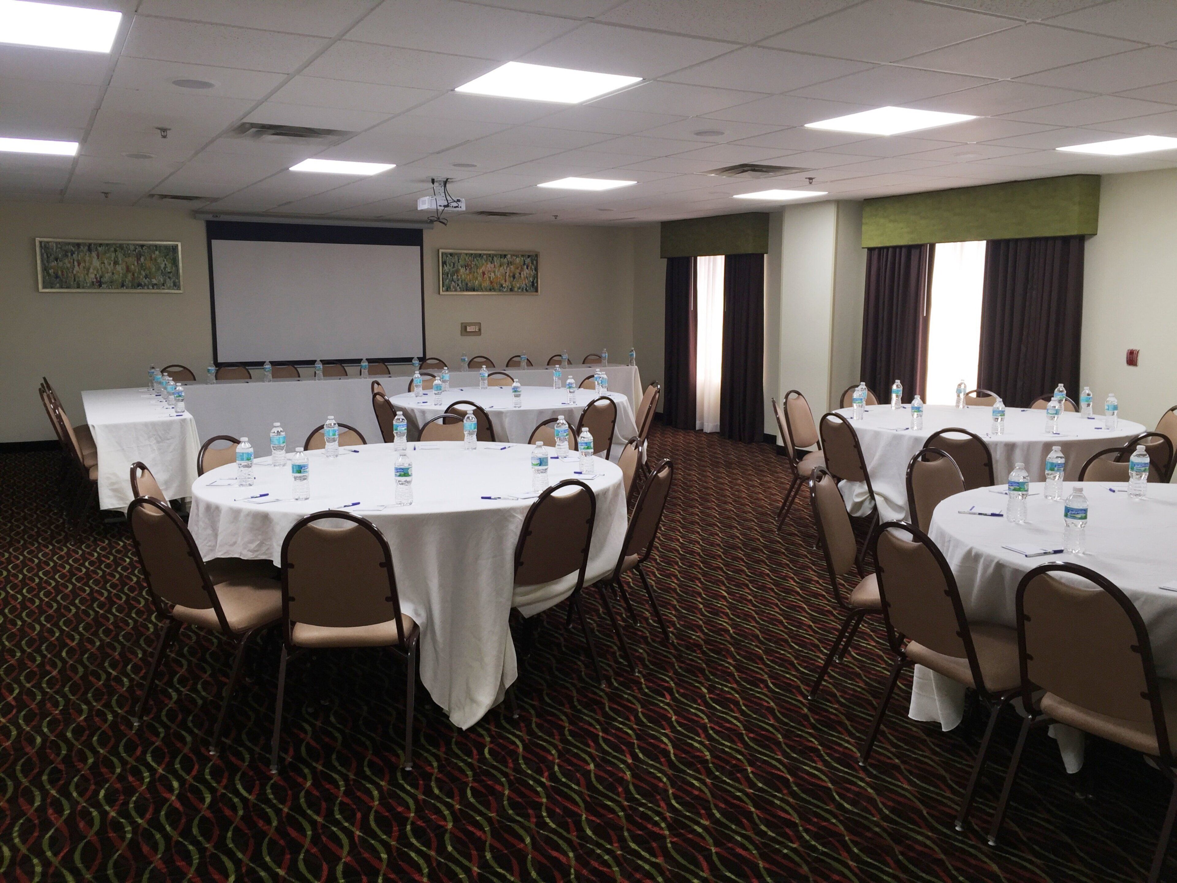 A conference room with round tables, chairs, water bottles, and a projector screen.