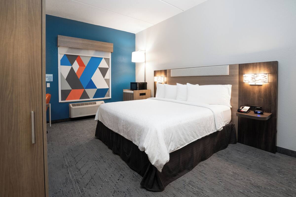 A hotel room with a large bed, bedside tables, a desk, and a wall-mounted TV.