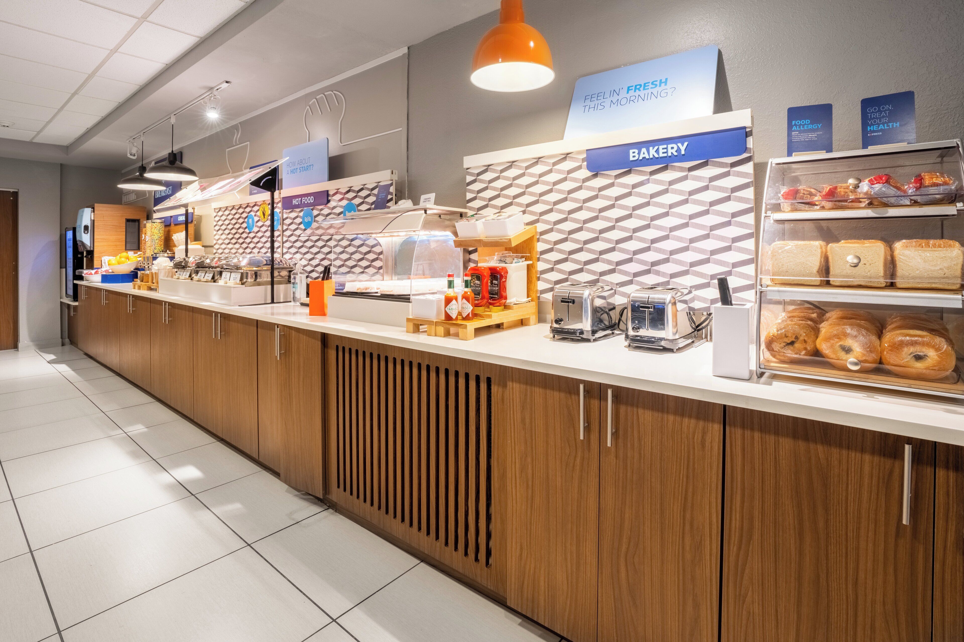 Mostrador de panadería con panes y pasteles varios, una máquina de café y dispensadores de condimentos.