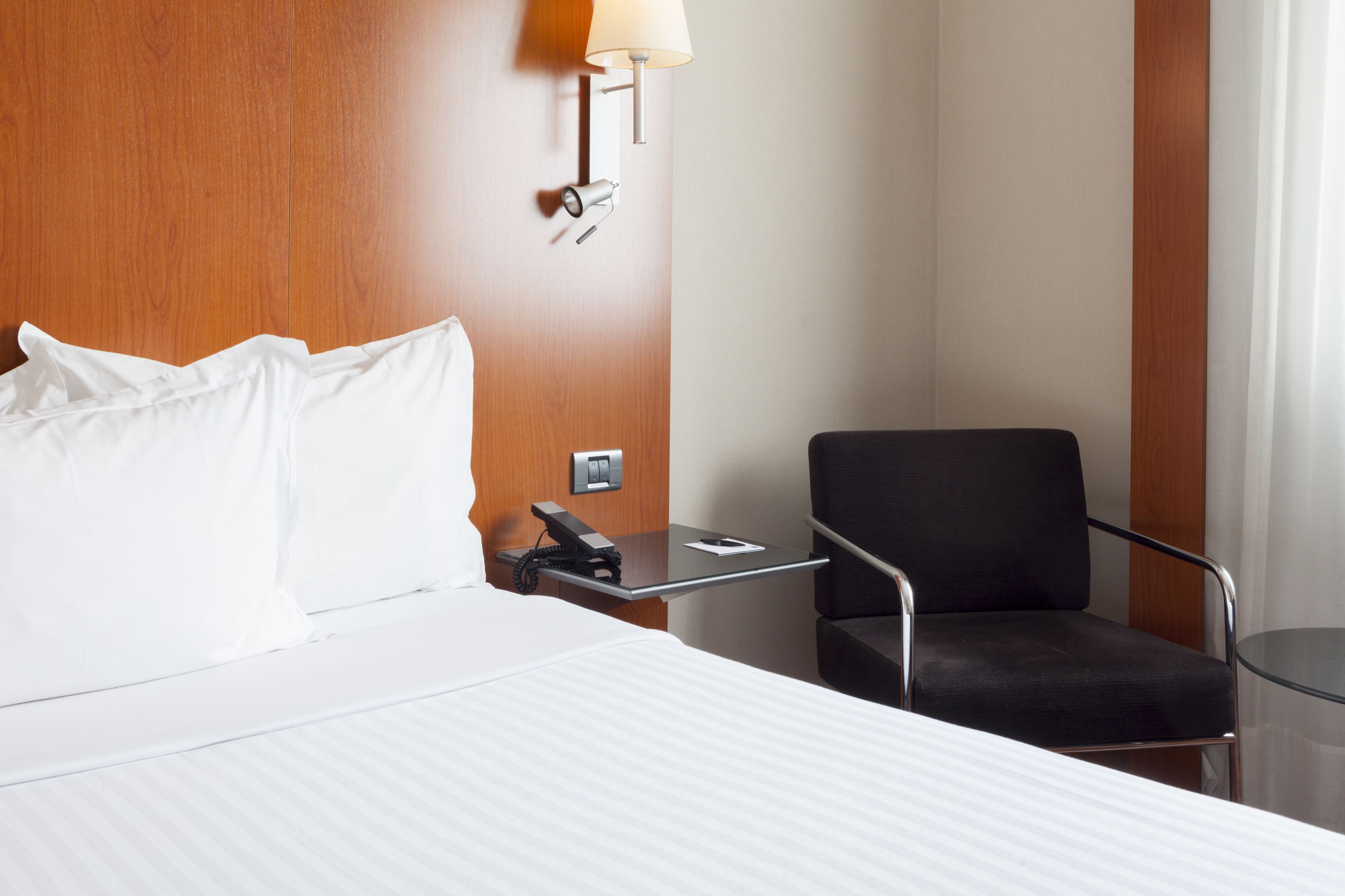 Una habitación de hotel con una cama, un escritorio con lámpara, una silla y un teléfono.