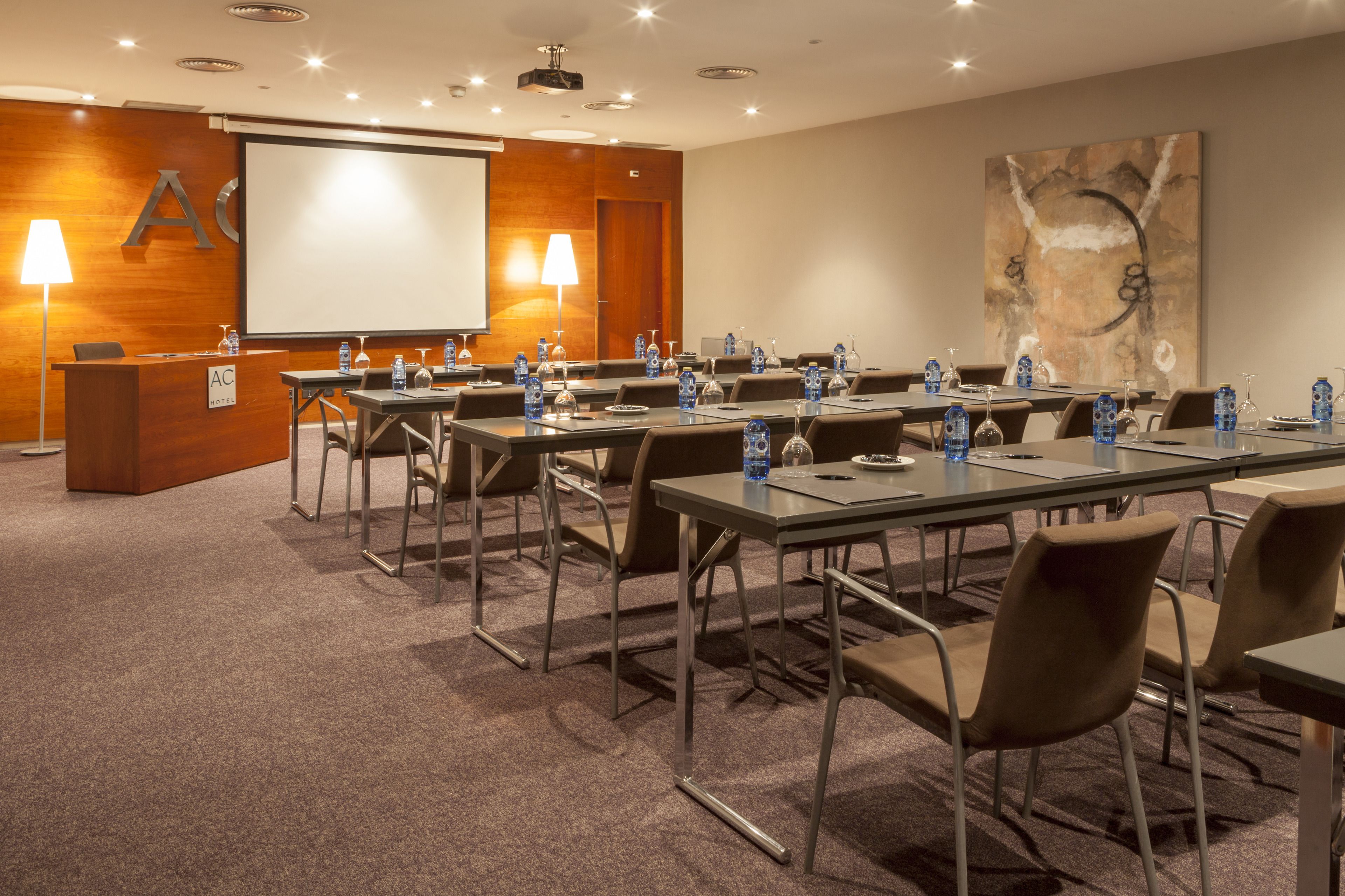 Un salón de conferencias con una pantalla grande, un atril y varias mesas con sillas.