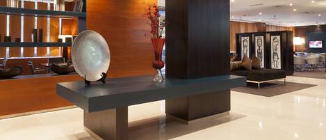 A modern reception area with a reception desk, a decorative glass bowl, a vase with red flowers, and a seating area with a sofa and chairs.