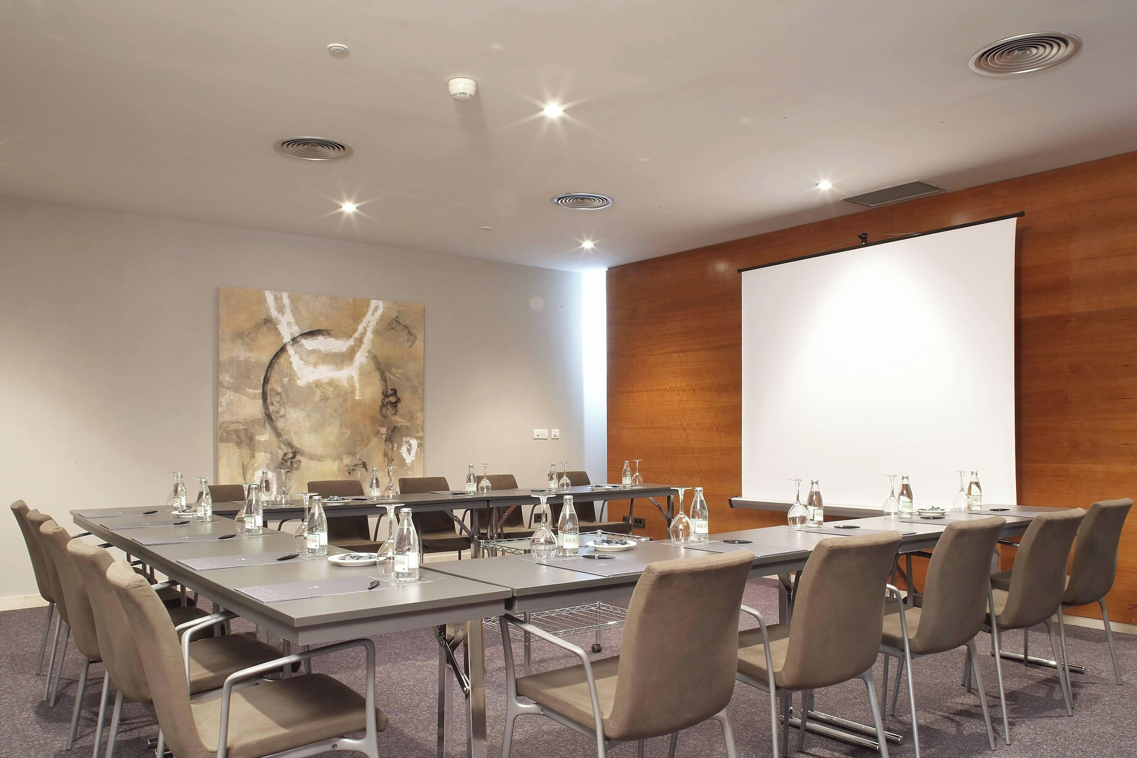 A conference room with a long table, chairs, water bottles, and a projector screen.