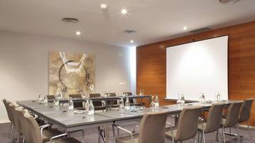 A conference room with a long table, chairs, water bottles, and a projector screen.