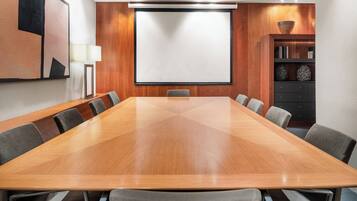A conference room with a large wooden table, grey chairs, a projector screen, and a cabinet with decorative items.