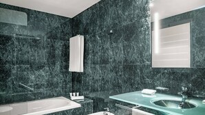 A modern bathroom with a bathtub, a sink, and a bidet. The walls are covered in dark marble tiles. - AC Hotel Badajoz by Marriott (Badajoz)